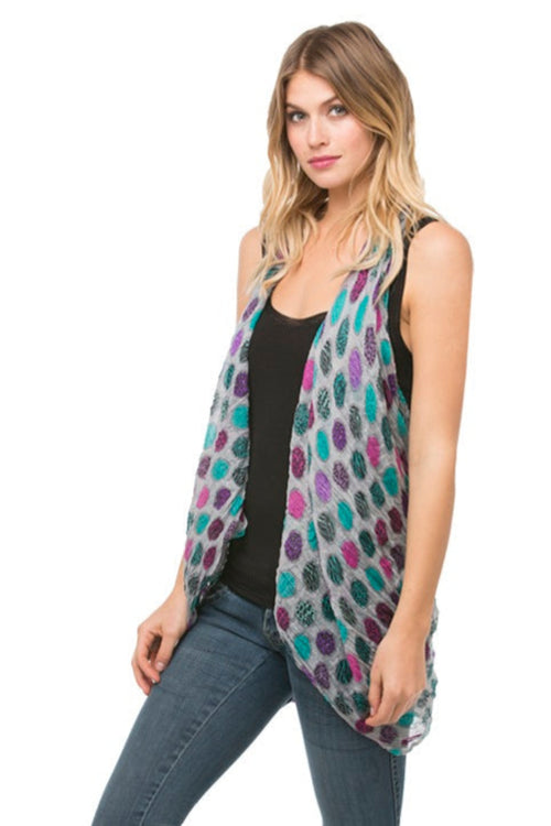 Woman wearing a printed dot pattern vest over a black top and jeans on a white background