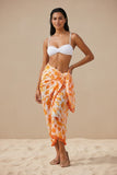 Model wearing a Subtle Luxury orange and white sunburst print sarong with tassel trim over a white bikini on sand