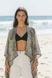 Model wearing a Subtle Luxury printed silk kimono jacket with a hi-low hemline by a tropical pool.